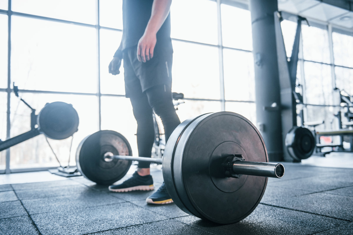 Strong young man in sportive clothes doing exercises with heavy weights in the gym.