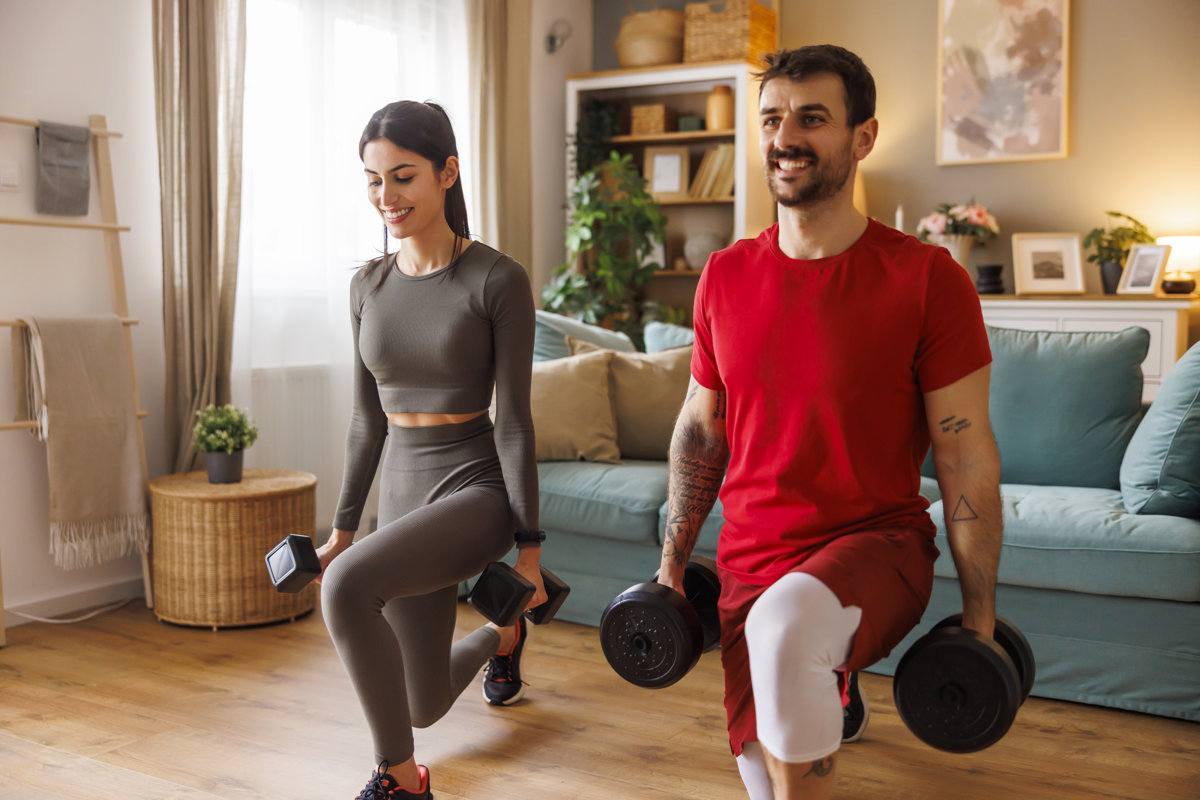 Active fit young couple doing dumbbell lunges exercise while working out together at home